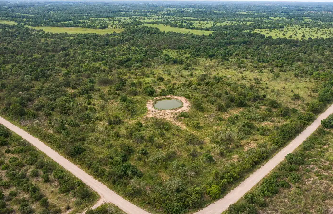 Aerial view of a large parcel of scrub, mixed woods and meadow bounded by two gravel county roads meeting at an angle