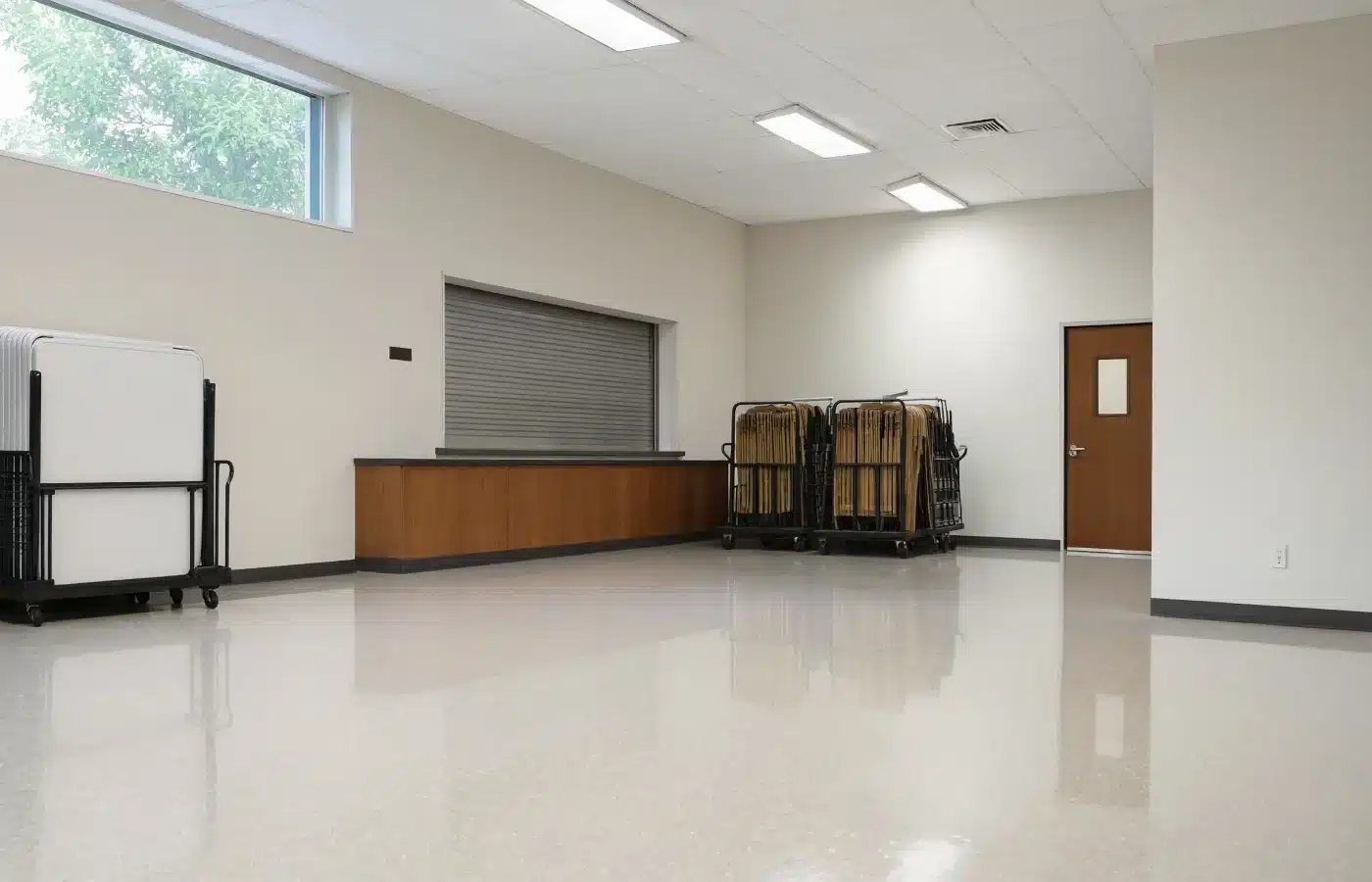 An empty church fellowship hall with folding chair carts along one wall and a closed kitchen serving counter