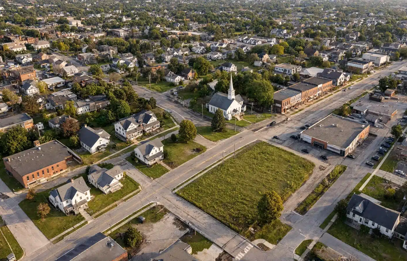 An aerial view of a small town showing houses, a church with a steeple, a commercial corner and a vacant lot