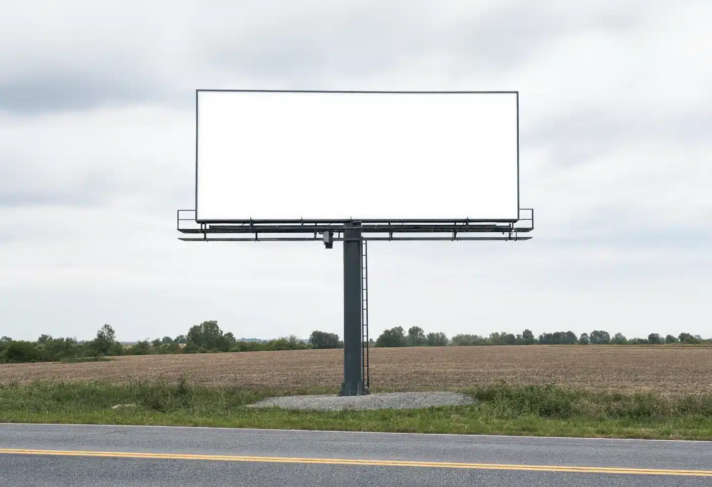 A blank billboard on a small gravel pad beside a rural highway, the kind of billboard easement donated to charity
