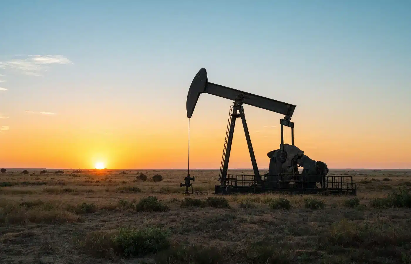 A pumpjack standing in open grassland with the sun on the horizon behind it