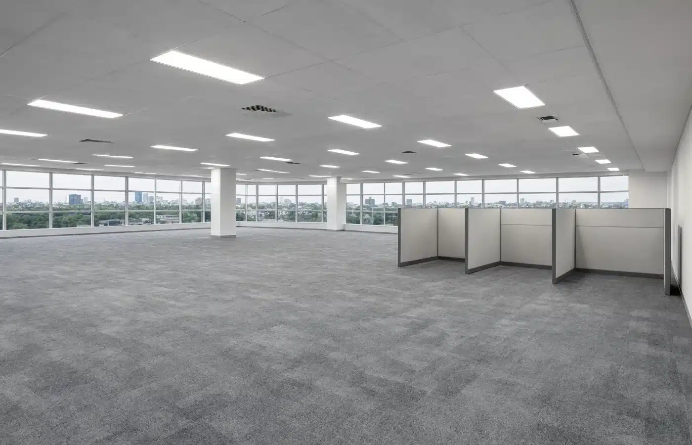 An empty open-plan office floor with wraparound windows, carpet tile and a few remaining cubicle panels