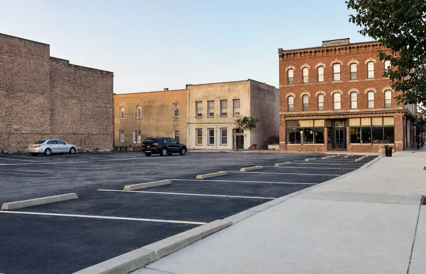 A striped downtown surface parking lot beside a row of brick commercial buildings
