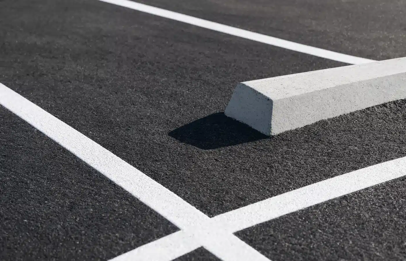 Close view of fresh white parking stripes and a concrete wheel stop on new asphalt