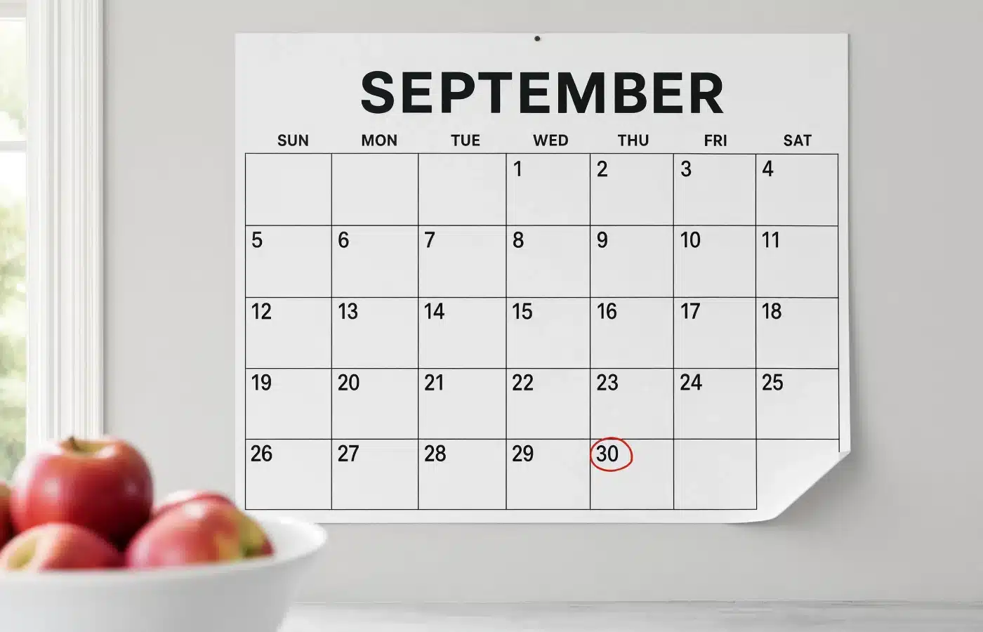A paper kitchen wall calendar with the end of the month circled in red marker