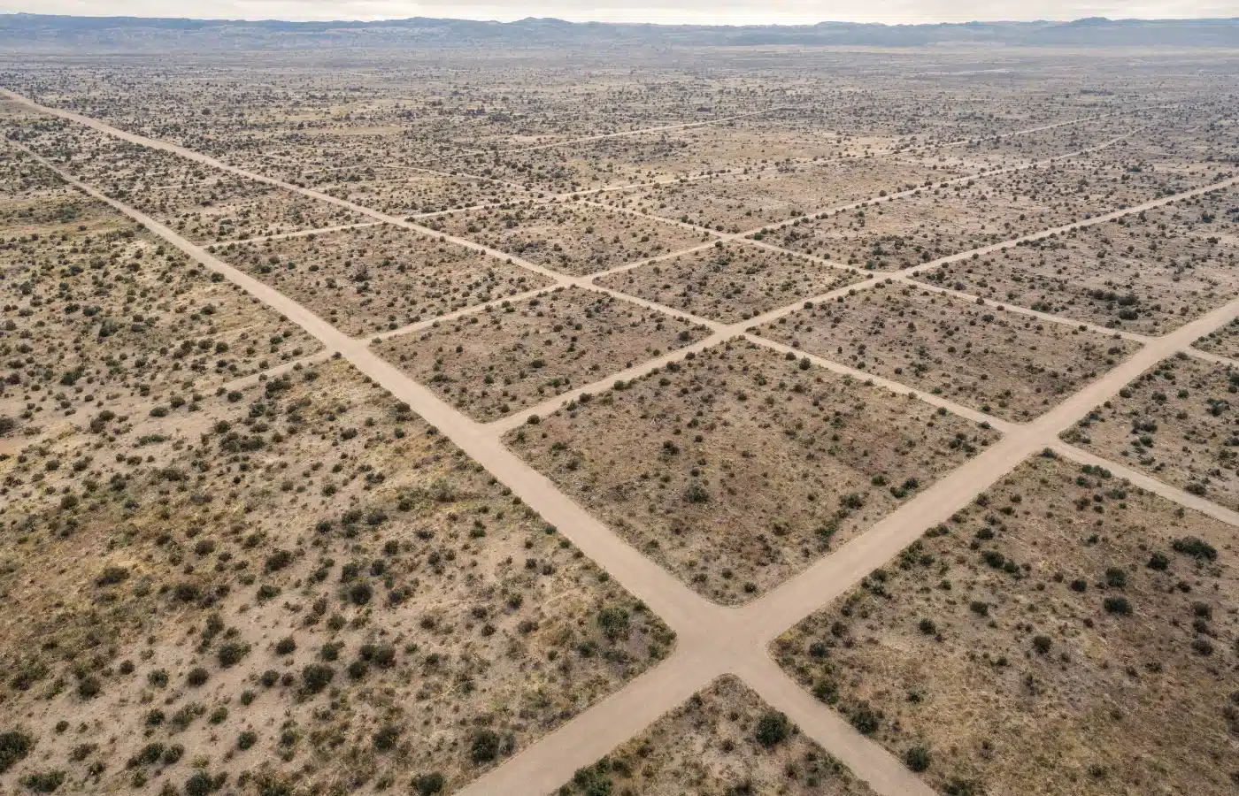 Aerial view of a paper subdivision in the desert: a grid of graded dirt roads and empty lots running to the horizon