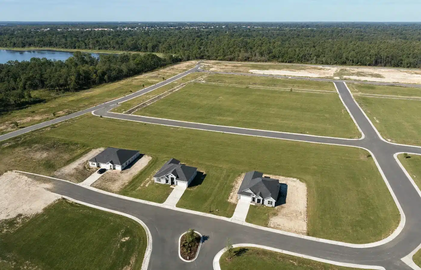Aerial view of an unfinished subdivision with paved streets in place and two dozen level grassy lots still empty